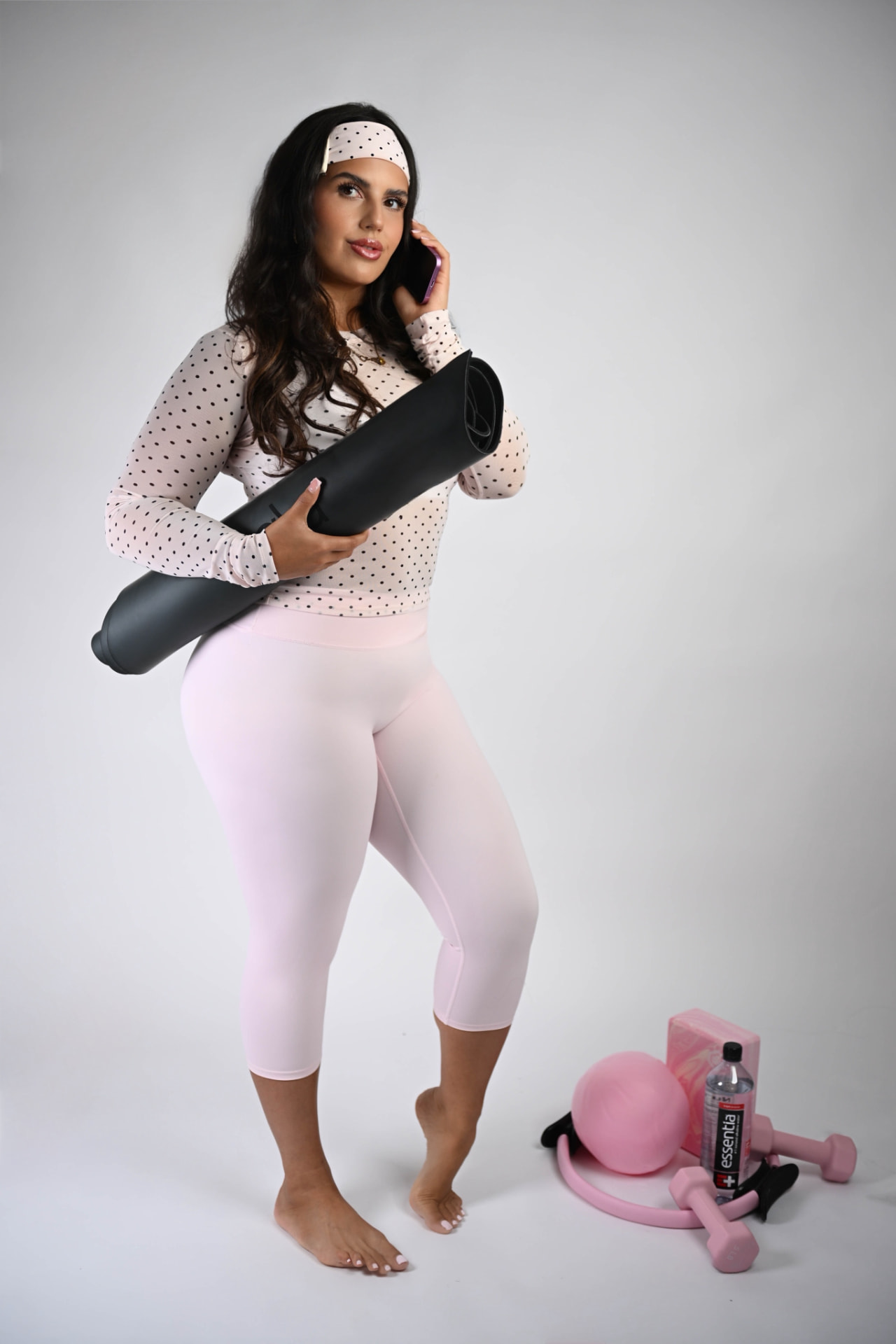 Founder in pink activewear holding a rolled mat while on the phone